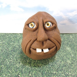 May include: A brown clay sculpture of a face with large blue eyes and a toothy grin.