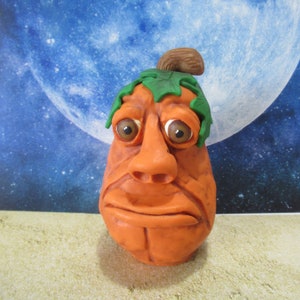 Op de afbeelding: Een handgemaakte oranje pompoen met een groen blad en een bruine steel, gebeeldhouwd in een gezicht met grote ogen en een fronsende mond.