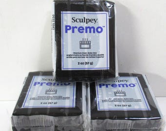 Może przedstawiać: Trzy prostokątne bloki czarnej gliny polimerowej Sculpey Premo, każdy indywidualnie owinięty w przezroczystą folię. Białe etykiety zawierają niebieski tekst, ikonę piekarnika oraz wagę 57 g (2 oz) wydrukowaną na froncie.