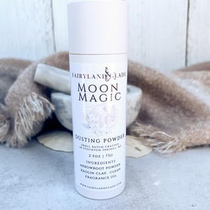 May include: A white cylindrical dusting powder container with a white cap. The label reads "Moon Magic Dusting Powder" with the brand name "Fairyland Glade". The ingredients and weight are also listed on the label. The container is 2.5 oz.