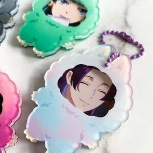 May include: A selection of anime-style character keyrings. Each keyring features a character portrait within a fluffy, animal-shaped frame. The frames are in various pastel colours, including green, blue, pink, and white, with a matching chain.