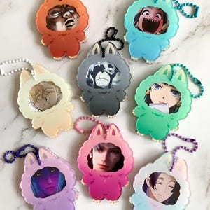 May include: A selection of acrylic keyrings in various colours. Each keyring has a cartoon animal design with a face inside. The keyrings are in shades of orange, blue, green, pink, purple, and light blue, each with a different image.
