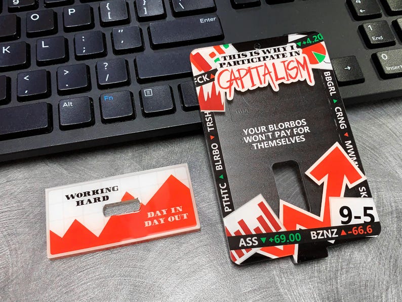 May include: Two red and white plastic cards with a graphic of a rising stock market. The text on the cards reads "Working Hard Day In Day Out" and "This is why I participate in Capitalism".