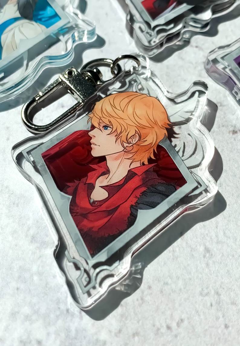May include: A clear acrylic keychain featuring a character with blond hair and a red shirt. The character is depicted in profile, looking to the left. The keychain has a silver metal ring.