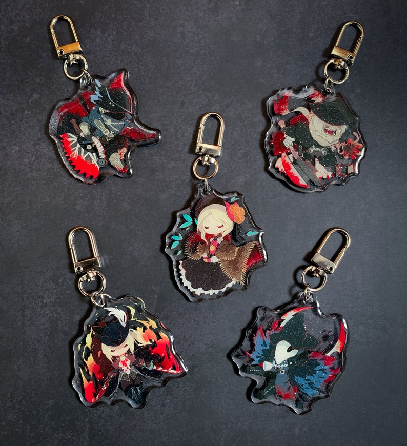 May include: Five colorful keychains featuring anime characters with black and white details. Each keychain has a silver metal ring and a clear acrylic background.