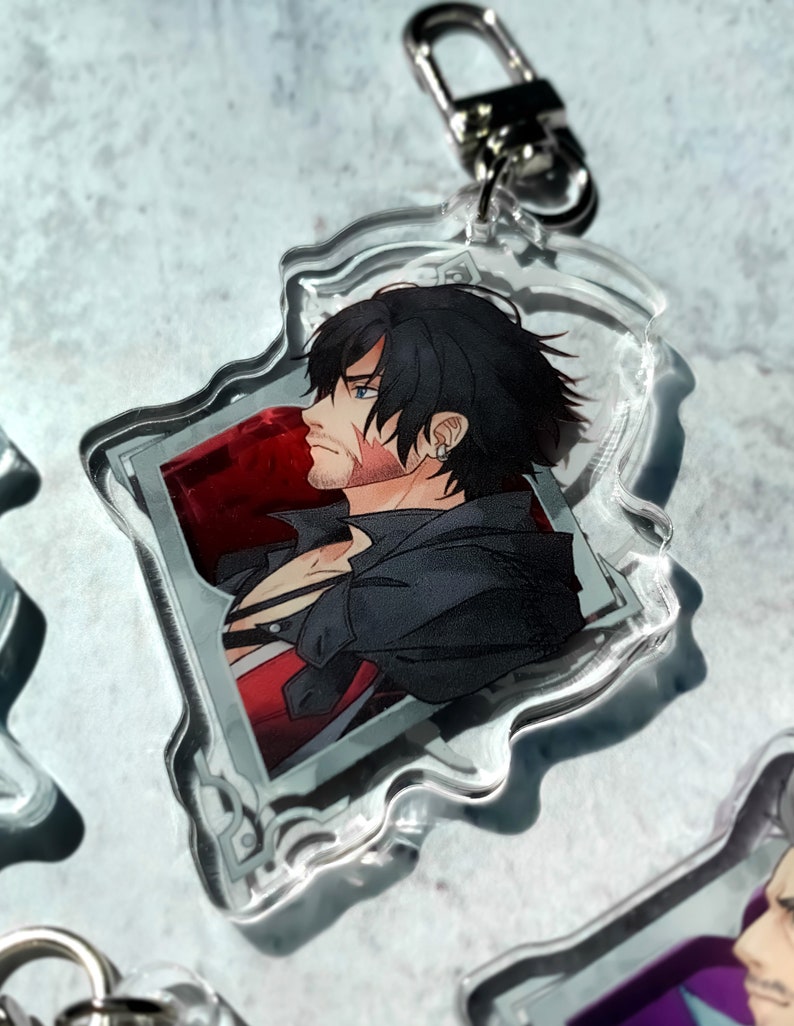 May include: A clear acrylic keychain featuring a character with black hair and a red and black outfit. The character is looking to the side and has a scar on their face. The keychain is shaped like a jagged rectangle with a silver metal ring.
