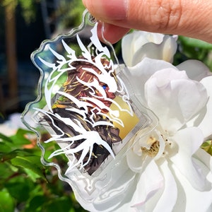 May include: A white and gold anime character keychain with a white dragon design. The keychain is made of clear acrylic and has a silver metal ring.