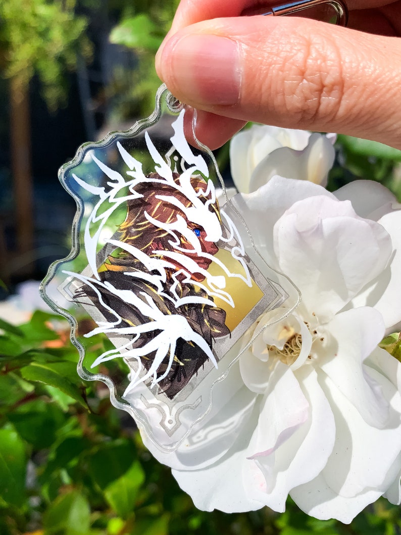 May include: A white and gold anime character keychain with a white dragon design. The keychain is made of clear acrylic and has a silver metal ring.