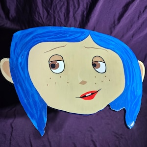 May include: A hand-painted wooden cutout of a girl with blue hair and a light brown complexion. The girl has brown eyes, a red mouth, and freckles.