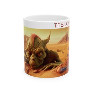 May include: White ceramic mug with a colorful image of a green, reptilian creature with red hair in a desert landscape. The text "TESLON" is printed in red on the top of the mug and "FRIEND" is printed in blue on the bottom.
