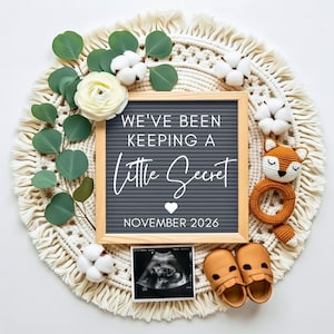 May include: A pregnancy announcement featuring a gray letter board with the text "WE'VE BEEN KEEPING A Little Secret NOVEMBER 2026." The board is surrounded by a macrame circle, flowers, and baby items, including a scan and small shoes.