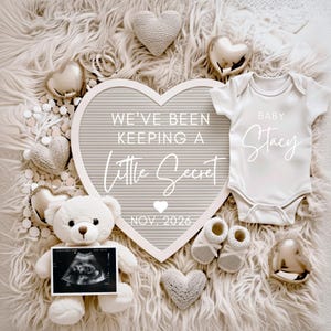 May include: A heart-shaped announcement board with the text "WE'VE BEEN KEEPING A Little Secret" and "NOV. 2026". A white babygrow with "BABY Stacy" is next to baby booties, a teddy bear holding an ultrasound image, and decorative hearts.