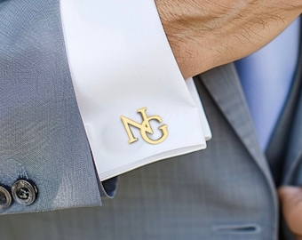May include: A gray suit jacket with a white shirt and a light blue tie. The cufflinks are gold and feature the initials "NG".