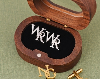 May include: A wooden box with a black velvet interior containing silver cufflinks with the initials "WRWR". Two gold cufflinks with the initials "NG" are on a green surface.