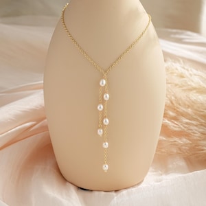 Puede incluir: Un collar de cadena dorada con una delicada gota de perlas. El collar presenta una cadena simple con una sola hebra de perlas que cuelga del centro.