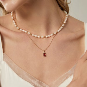 Pode incluir: Um colar de corrente de ouro com um pingente de pedra vermelha e um colar de pérolas sobreposto.