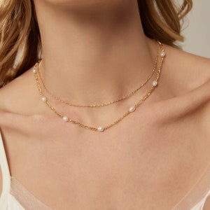 Op de afbeelding: Een gouden ketting met een delicate ketting en kleine parel accenten. De ketting is gelaagd met een dunnere ketting.