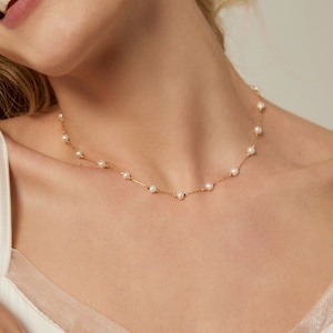 May include: A delicate gold chain necklace with small white pearls. The necklace is simple and elegant, perfect for everyday wear.