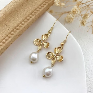 May include: Gold flower dangle earrings with a white pearl drop. The earrings have a delicate floral design with a small rhinestone in the center of each flower.