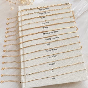 以下が含まれることがあります： 14種類のゴールドチェーンがそれぞれ名前でラベル付けされた白いカード。チェーンには、ペーパークリップ4mm、ペーパークリップ2mm、ロープ、ビーズL、デイジー、ヘリンボーン3mm、ヘリンボーン2mm、ツイスト、スネークビーズ、ラウンドスネーク、ビーズ、リップ、ボックスが含まれています。