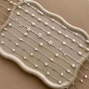 May include: A set of ten delicate pearl necklaces with silver chains. Each necklace features a different pearl size and style, including some with small flower charms.