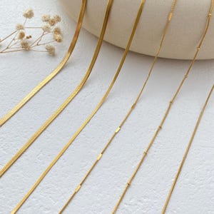 May include: A set of six gold chain necklaces with different styles, including a snake chain, a box chain, and a beaded chain.