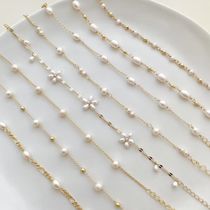 Puede incluir: Un conjunto de siete delicados collares de cadena dorada con detalles de perlas y flores. Los collares presentan una variedad de tamaños y estilos de perlas, incluyendo pequeñas perlas redondas, perlas ovaladas más grandes y delicados abalorios de flores.