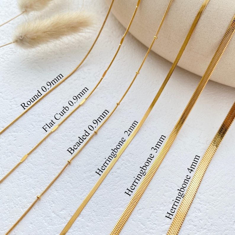 May include: A close-up of six gold chains of different styles and widths. The chains are labeled with their names and thicknesses in millimeters: Round 0.9mm, Flat Curb 0.9mm, Beaded 0.9mm, Herringbone 2mm, Herringbone 3mm, and Herringbone 4mm.