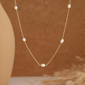 Pode incluir: Um delicado colar de corrente de ouro com cinco pequenas pérolas brancas espaçadas uniformemente ao longo da corrente.