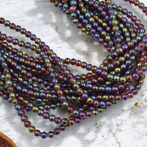 May include: Strands of iridescent beads in shades of purple, bronze, and green. The small, round beads are strung together, creating a textured and colorful display. These beads are perfect for jewelry making.