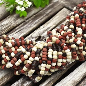 May include: A strand of small, round beads in white, brown, and red colors. The beads are made of glass and have a slightly irregular shape.