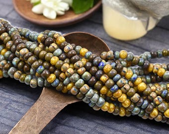 May include: A close-up of a strand of small, round, ceramic beads in shades of brown, blue, and yellow. The beads are arranged in a loose pile on a wooden surface.