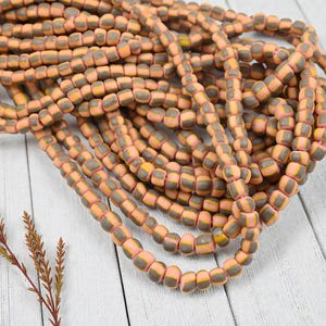 May include: Strands of handmade beads in a mix of colors. The beads are a mix of peach, gray, and yellow. The beads are strung together to create a necklace or bracelet. The beads are on a white wooden surface.