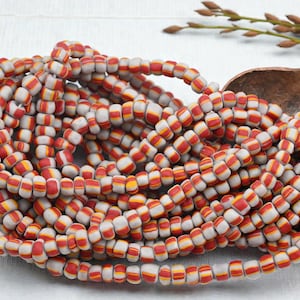 May include: Strands of gray and red striped beads. The beads are cylindrical with a white base and red and yellow stripes. The beads are strung together, forming a necklace or bracelet.
