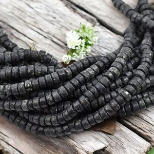 May include: A strand of black, round, and slightly textured beads. The beads are strung together to form a long necklace.