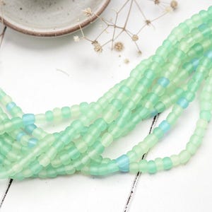 May include: Multiple strands of small, round, matte-finish beads in varying shades of mint green and pale turquoise. The beads have a soft, frosted texture and are arranged in a loose, flowing cluster, showcasing their consistent size and shape.