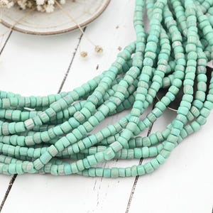 May include: A collection of mint green, cylindrical beads with a ribbed texture, arranged in multiple strands. The beads feature a matte finish and a consistent shape, creating a uniform appearance across the entire length of the strands.
