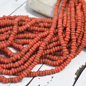May include: A large collection of coral-colored, disc-shaped beads strung together on multiple strands. Each bead features a textured, porous surface and a uniform, flattened circular shape, creating a dense, vibrant pile of orange-red jewelry components.