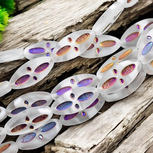 May include: A strand of oval-shaped glass beads with iridescent purple, pink, and gold accents. The beads have a frosted finish and are strung together on a clear thread.