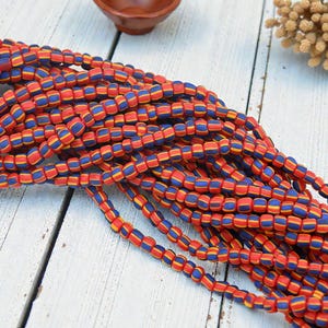 May include: Strands of colorful beads in red, blue, and yellow. The beads are small, rectangular, and arranged in a pattern of stripes. The beads are likely for jewelry making or crafting.