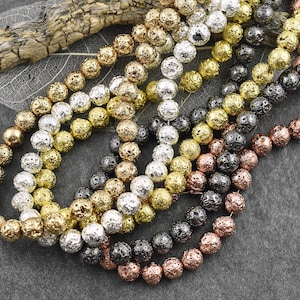 May include: A collection of lava rock beads in various metallic finishes, including gold, silver, black, and copper. The beads are round and have a porous texture.