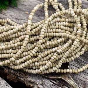 May include: A close-up of a pile of off-white round beads. The beads are small and have a slightly rough texture.