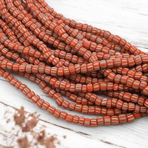 May include: Strands of orange and gray striped beads. The beads are cylindrical with a series of white stripes. The beads are strung together, creating a textured and colorful display. The beads are likely used for jewelry making or crafting.