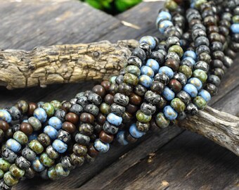 May include: A strand of small, round, multi-colored glass beads. The beads are a mix of brown, black, blue, and green with gold flecks. The beads are arranged in a coil on a wooden surface.