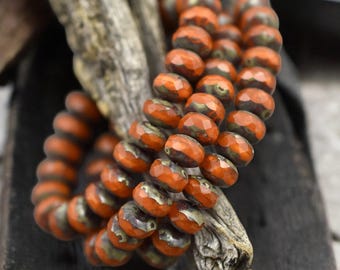May include: Close-up of a strand of orange and dark-toned faceted beads. The beads are strung together, creating a spiral and a layered effect. The beads are resting on a piece of weathered wood.