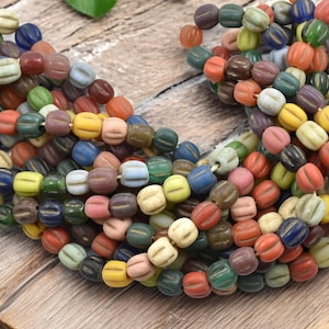 May include: A strand of colorful glass beads with a textured, ribbed surface. The beads are a mix of blue, green, yellow, red, and white.