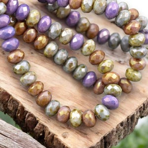 May include: A strand of iridescent glass beads in shades of purple, brown, and green. The beads are faceted and have a slightly irregular shape.