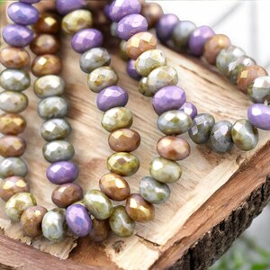 May include: A strand of iridescent glass beads in shades of purple, gold, and green. The beads are faceted and have a slightly irregular shape.