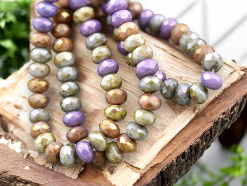 May include: A strand of iridescent glass beads in shades of purple, gold, and green. The beads are faceted and have a slightly irregular shape.