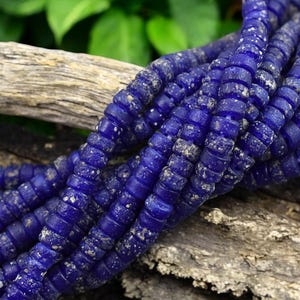 May include: A strand of blue glass beads with a textured surface. The beads are small and round, and they are strung together on a clear thread.